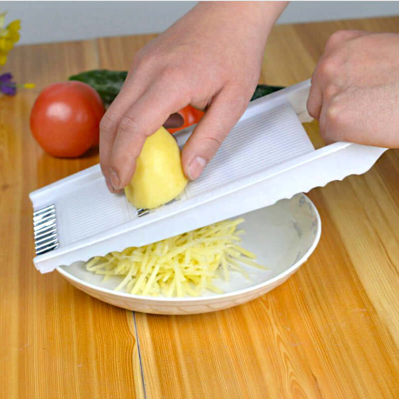 Hands using a multifunctional kitchen grater to shred a potato into thin strips on a plate.