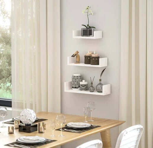 White wood wall-mounted shelf set displaying decorative items in a modern dining room setting with a wooden table.