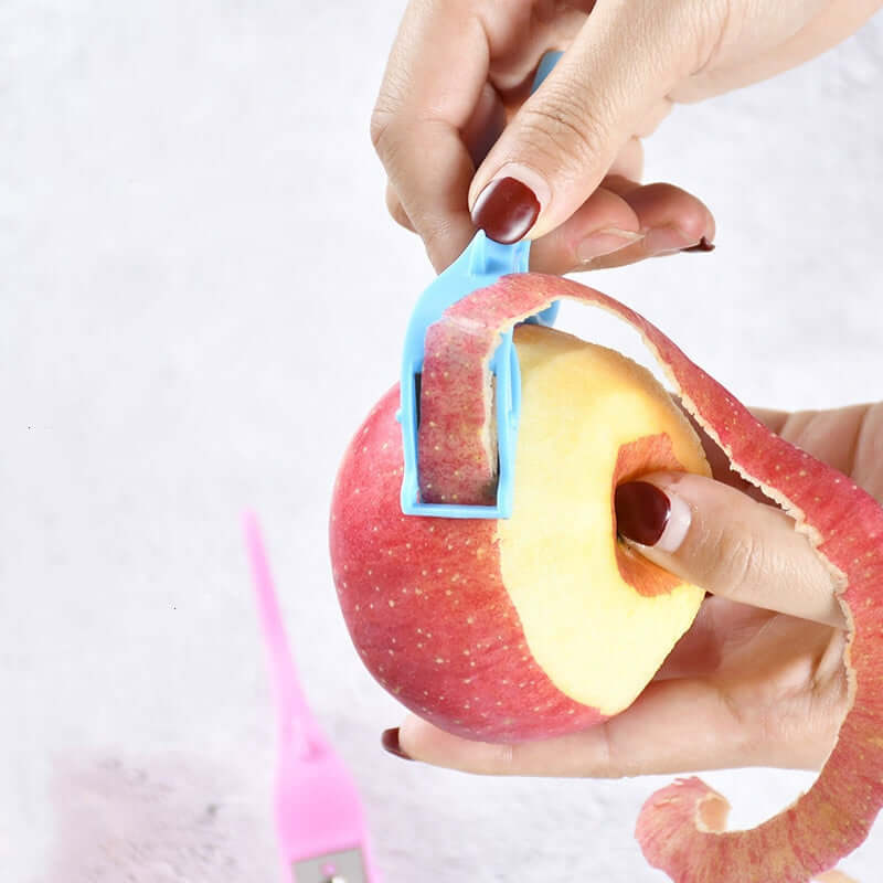 Multifunctional fruit peeler in use, peeling an apple with a blue finger ring scraper.