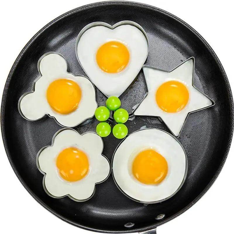 5Pcs stainless steel egg mold set shaped eggs in heart, star, flower, and round designs in frying pan.