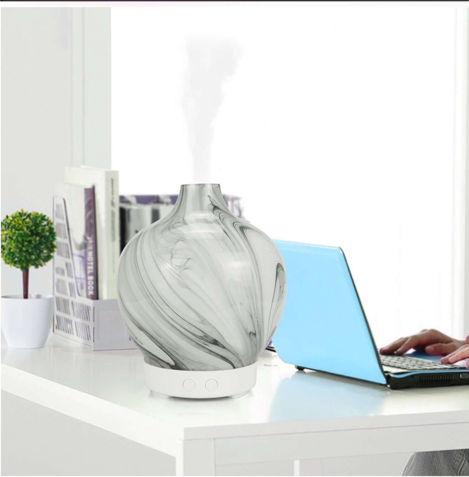 Glass aroma diffuser humidifier on a desk next to a laptop, adding style and soothing scents to a workspace.