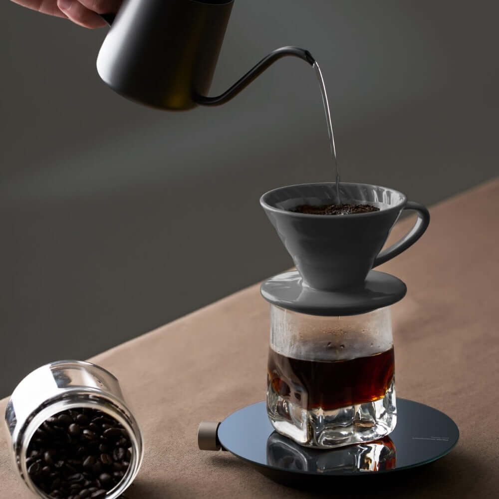 Coffee brewing process with a smart kettle pouring over grounds in a gray filter cone.