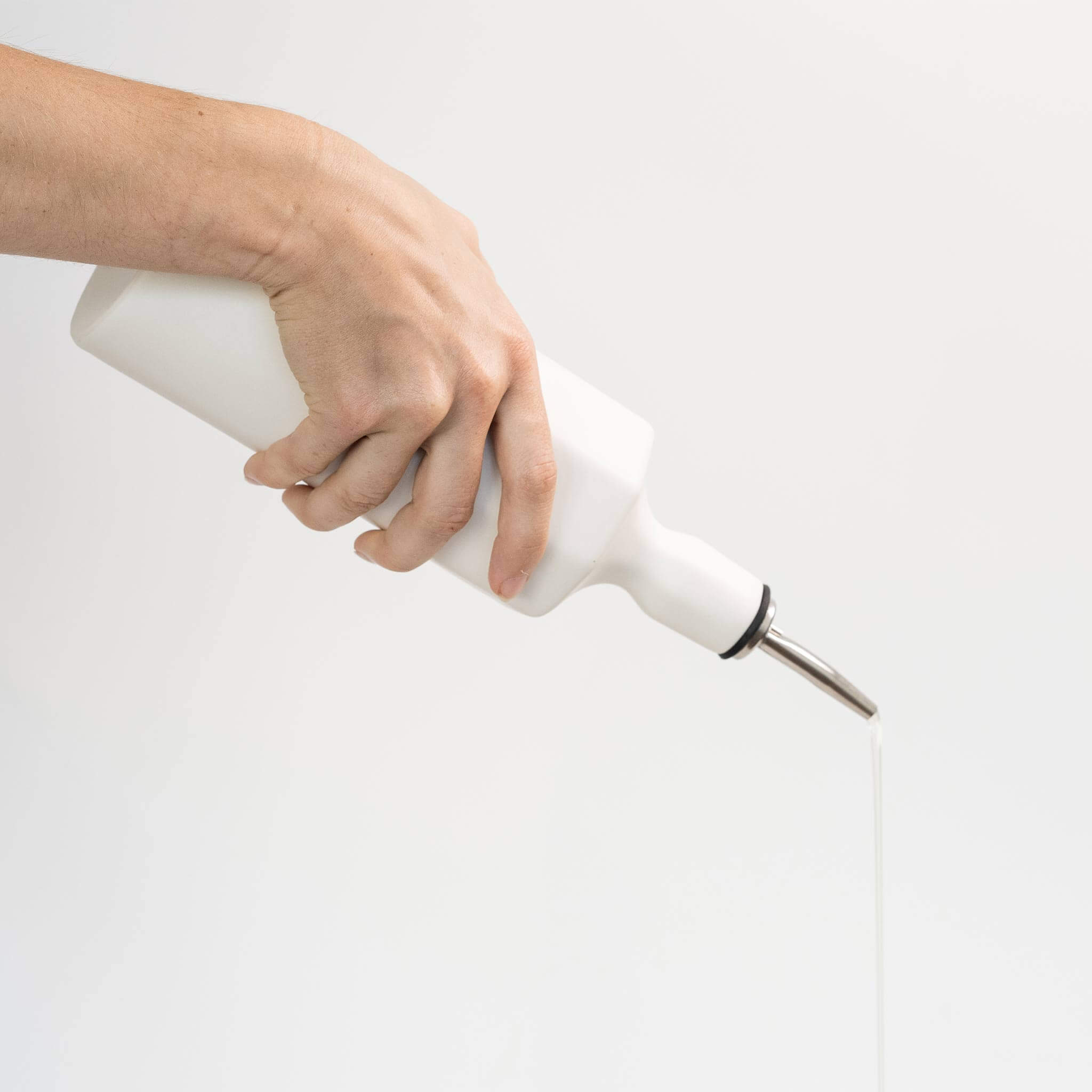 Hand pouring from a ceramic olive oil dispenser with a sleek design on a white background.