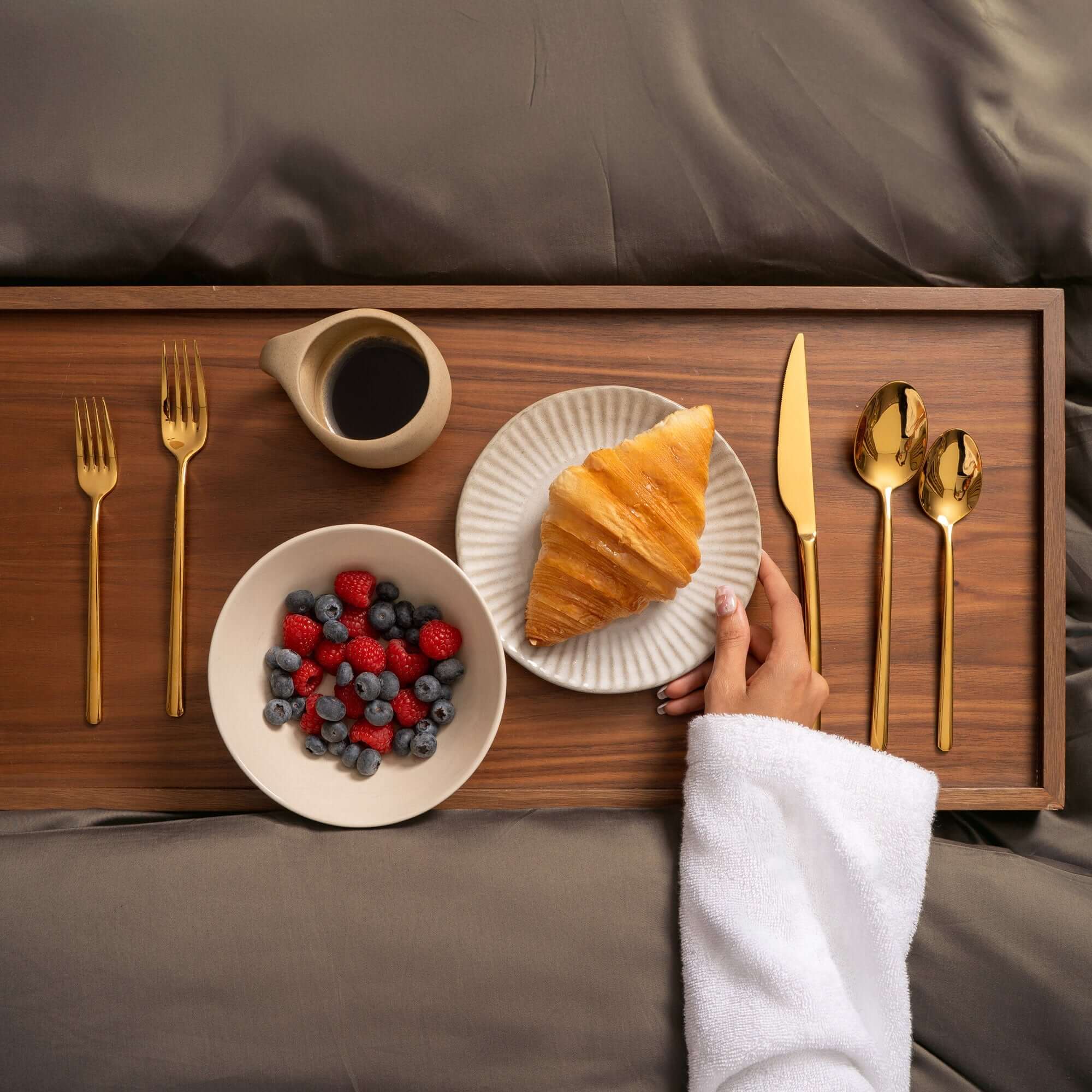 Emilia Mirror 20-Piece Flatware Set arranged on a wooden tray with breakfast items, featuring gold mirror-polished finish.