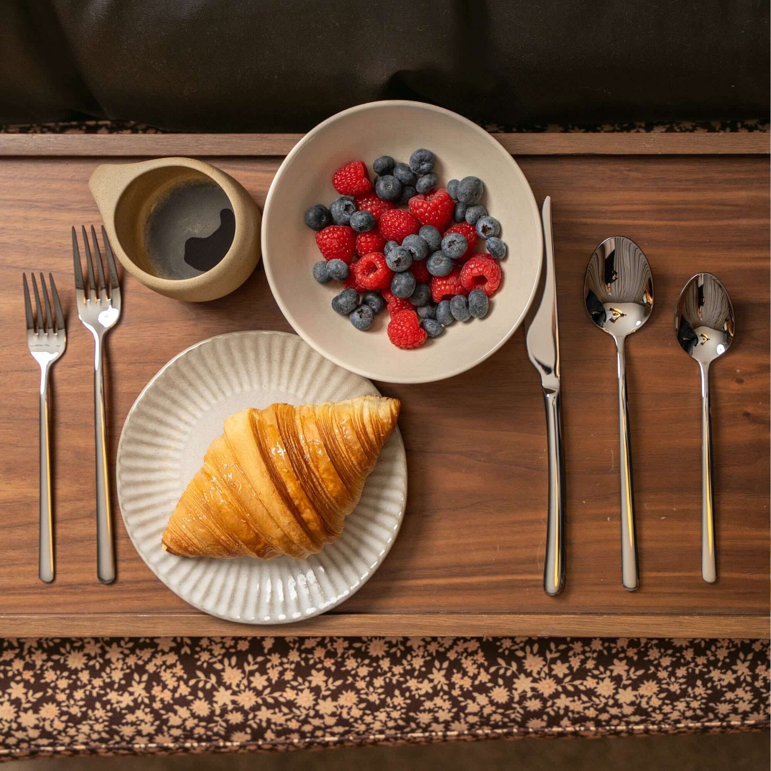 Emilia Mirror 20-Piece Flatware Set with croissant and berries on a wooden table.