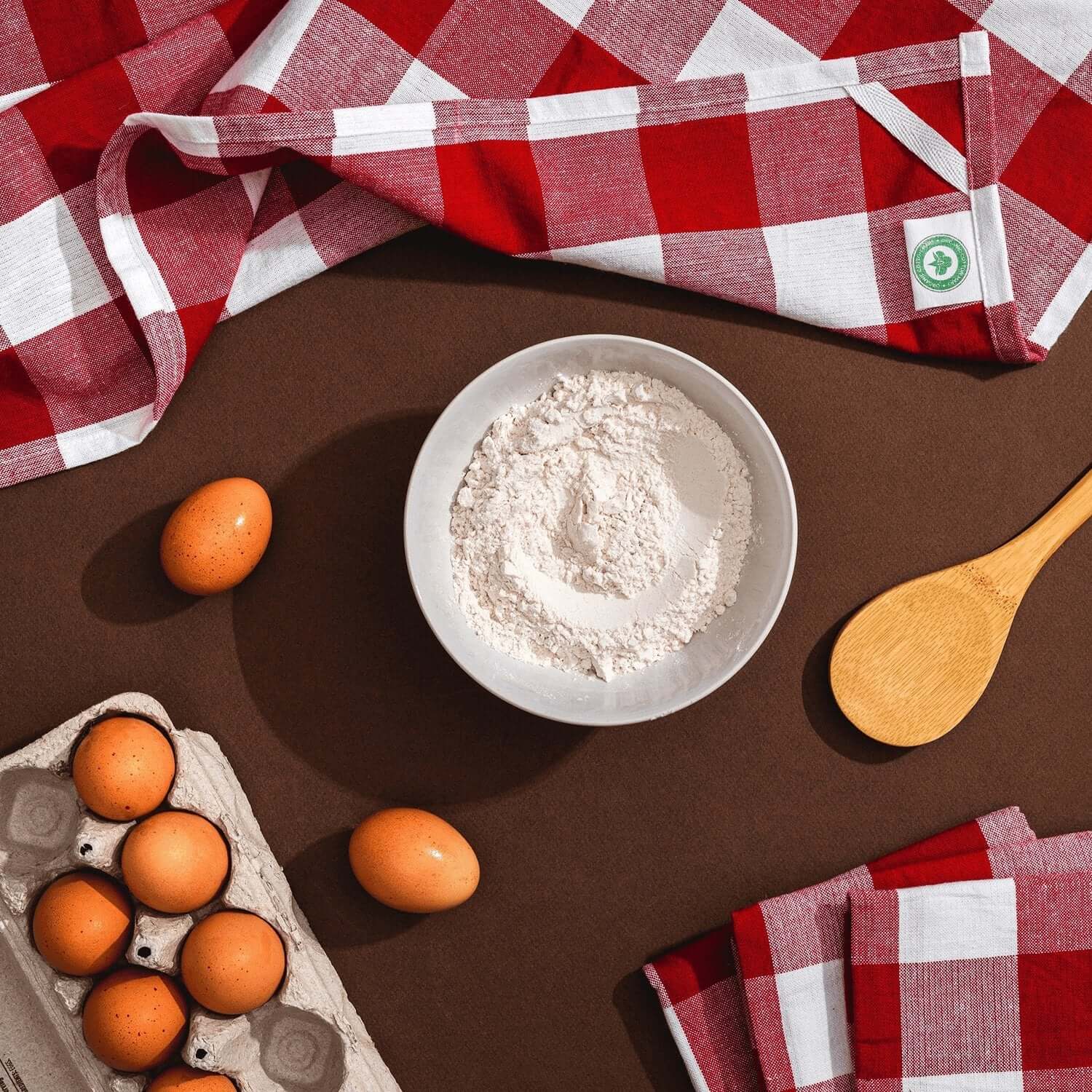 Plaid Kitchen Towels on a kitchen counter with flour, eggs, and a wooden spoon, showcasing style and functionality.