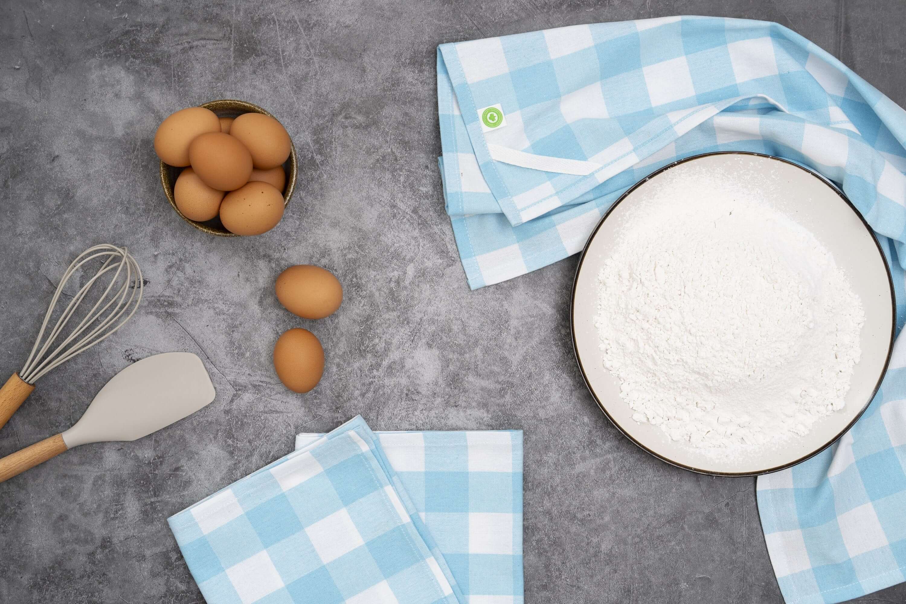 Plaid Kitchen Towels neatly arranged with eggs and flour on a gray surface, showcasing style and functionality.